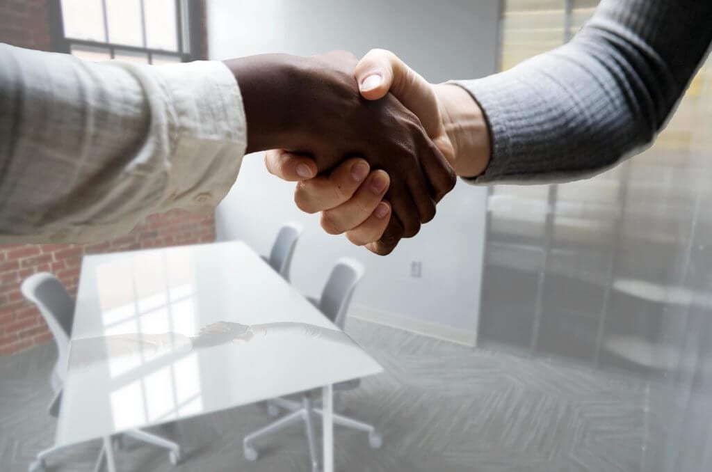 People handshaking in a meeting room with a table and chairs