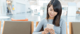 A woman sits with a smartphone and uses a mobile hotel application, mobile version